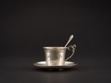 une tasse en argent contenant une cuillère, posée sur une soucoupe