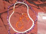 des colliers de perles violettes et blanches et un sac en plastique posés sur un lit