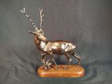 sculpture en bronze représentant un cerf, posée sur un socle en bois, sur fond noir