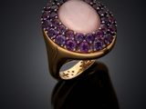 a close up of a ring with a pink stone surrounded by purple stones