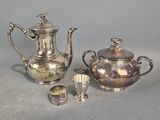 trois théières et tasses en argent posées sur une table devant un fond gris