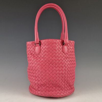 a pink handbag with a woven handle on a grey background