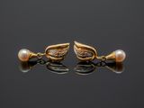 a pair of gold earrings with pearls on a black surface