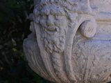 a stone vase with a bird on it in front of a bush