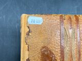 an old book with a brown leather cover sitting on top of a wooden table
