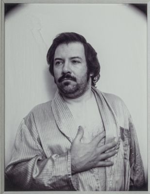 photographie en noir et blanc d'un homme en robe, les mains posées sur la poitrine
