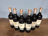 six bottles of wine are lined up in a row on a wooden table