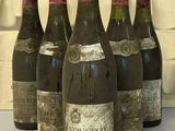Six bouteilles de vin sont alignées sur une table devant un mur de briques.