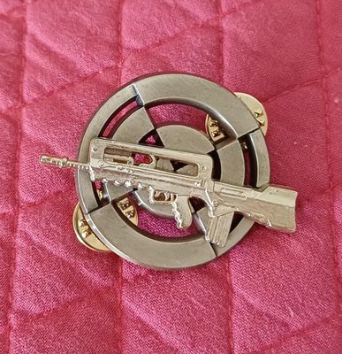 une broche en métal représentant un pistolet, posée sur une couette rose