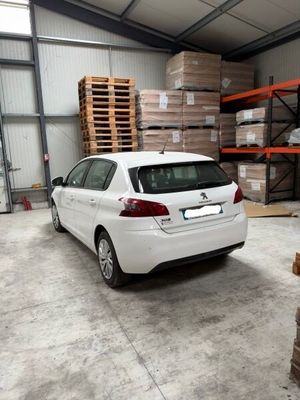 une voiture blanche garée dans un entrepôt, à côté d'une pile de palettes