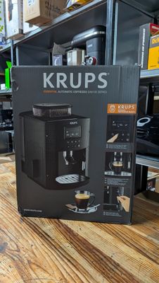 une boîte contenant une cafetière Krup posée sur une table en bois
