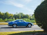 a blue car driving down the street next to a bush