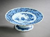 une assiette bleue et blanche posée sur un socle, sur une table