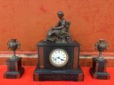 une statue de femme assise sur une table à côté de trois vases et d'une horloge