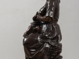 an antique bronze statue of a woman sitting on a rock