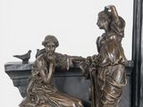 a statue of two women sitting on a bench with a bird perched on top of it