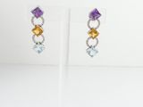 a pair of earrings with multi colored stones on a stand