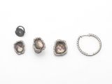 trois paires de boucles d'oreilles, une bague et une bague posées sur un fond blanc