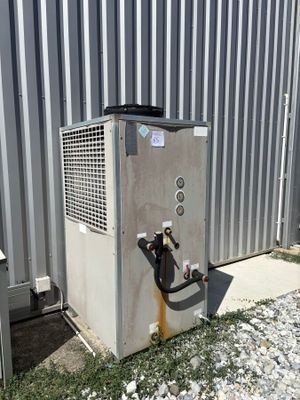 un climatiseur installé à l'extérieur d'un bâtiment métallique, auquel est raccordé un tuyau