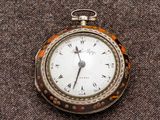 une montre de poche en argent posée sur une surface marron
