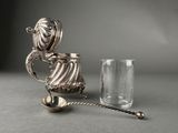a silver teapot and a glass on a table