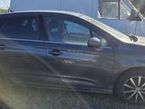 a small grey car parked in a field with a trailer in the background