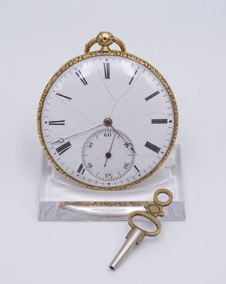 une petite montre de poche blanche avec une clé, posée sur un socle