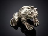 un gros plan d'une figurine de grenouille en argent posée sur une surface noire