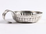 une vieille coupe en argent munie d'une anse, posée sur une surface blanche