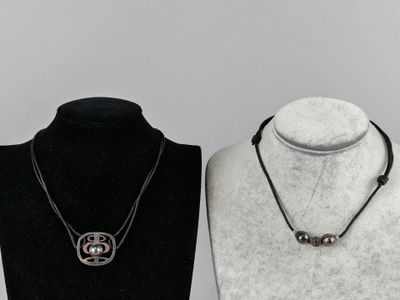 deux colliers posés sur un présentoir à mannequin, sur fond noir et blanc