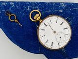 une montre de poche en or posée sur une pierre bleue