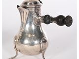 une cafetière en argent avec une poignée noire, posée sur un socle