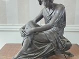 statue d'une femme assise sur une table en bois, les mains posées sur les genoux