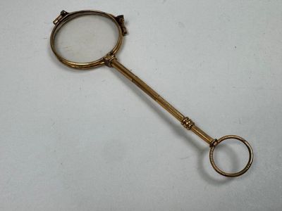brass plated magnifying glass with handle on a white surface