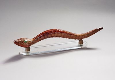 une sculpture en verre représentant un serpent, posée sur un socle transparent