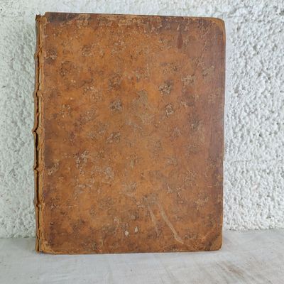 un vieux livre posé sur une table à côté d'un mur blanc