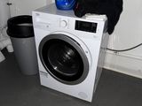 une machine à laver sur laquelle est posée une bouteille de lessive, à côté d'une poubelle