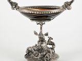un plat ancien en argent orné d'un oiseau, posé sur un socle