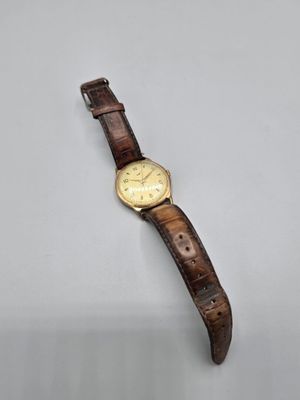 une montre en or avec un bracelet en cuir marron posée sur un fond blanc