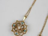 a close up of a gold necklace with a pearl pendant on it