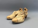 une paire de chaussures beiges ornées de boucles, posées sur une surface grise