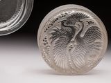 un objet en argent orné d'un oiseau, à côté d'un récipient en verre
