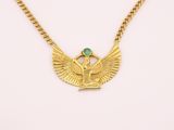 a gold necklace with an egyptian winged pendant and a green stone