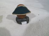 une petite statue représentant une personne coiffée d'un chapeau, assise sur un rocher