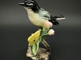 une figurine représentant un oiseau perché sur une branche, entouré de fleurs