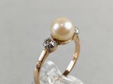 a close up of a pearl and diamond ring on a clear surface