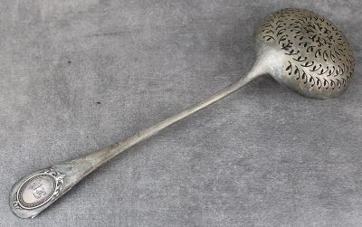 une cuillère ancienne en argent avec un manche, posée sur une surface grise