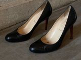 une paire de chaussures à talons hauts noires posées sur un sol en béton, près du mur