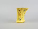 a yellow vase with flowers on it sitting on a white surface