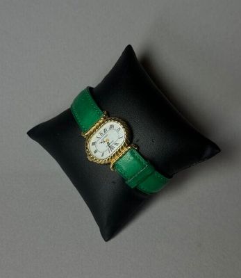 un oreiller noir orné d'une bande verte et sur lequel repose une montre blanche